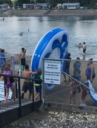 A person holds a spotted crappie fish up by a lake on a sunny day.