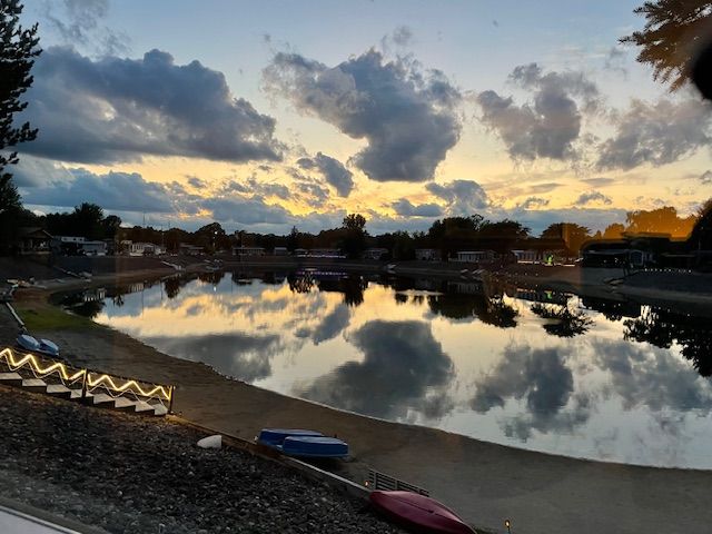 A calm lake reflects a sunset sky with scattered clouds, with canoes and lit steps along the shore.