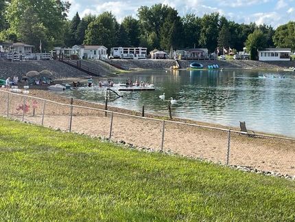 A sandy beach with a swimming area, floating platforms, and small homes on a hill overlooking the water.