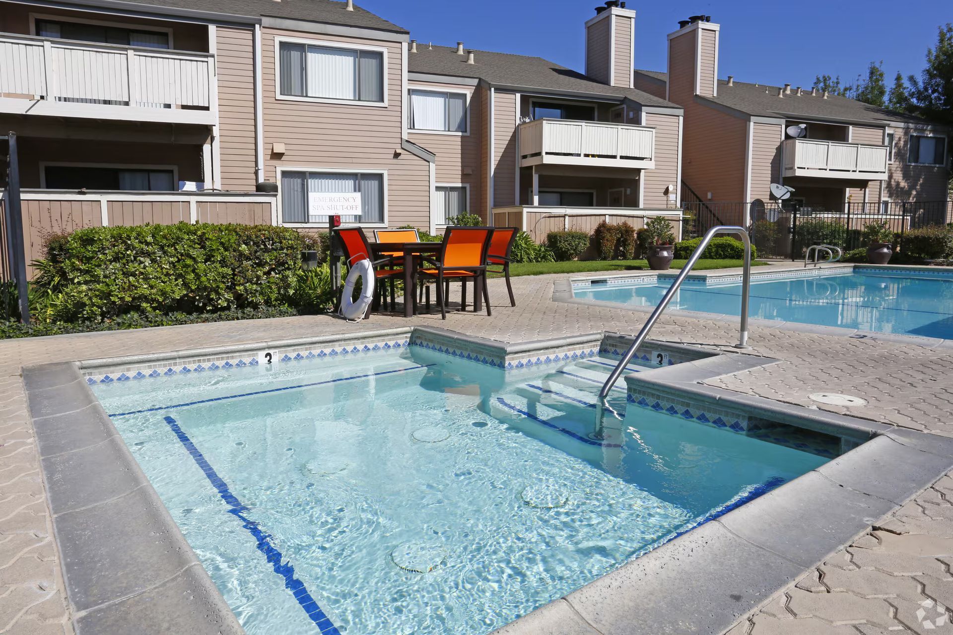 Apartment pool with hot tub, lounge chairs, and a swimming lane under a clear sky