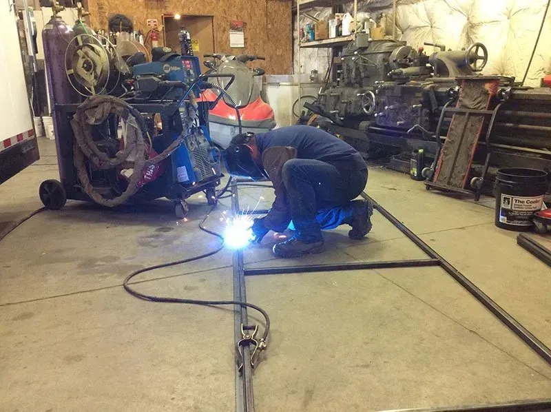 A man is welding a piece of metal in a garage