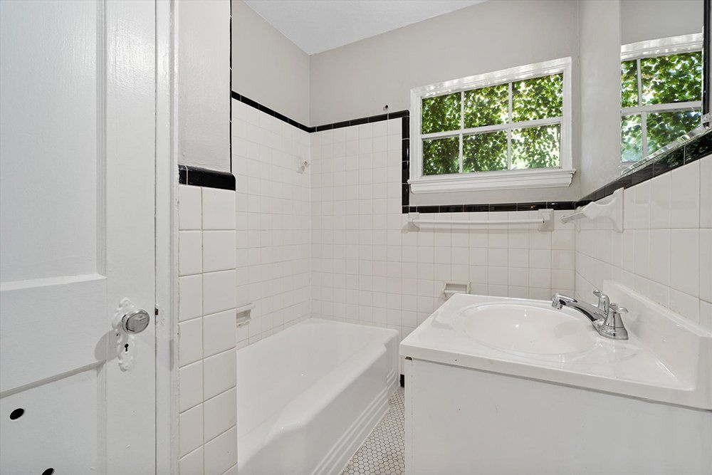 A bathroom with a tub , sink , mirror and window.