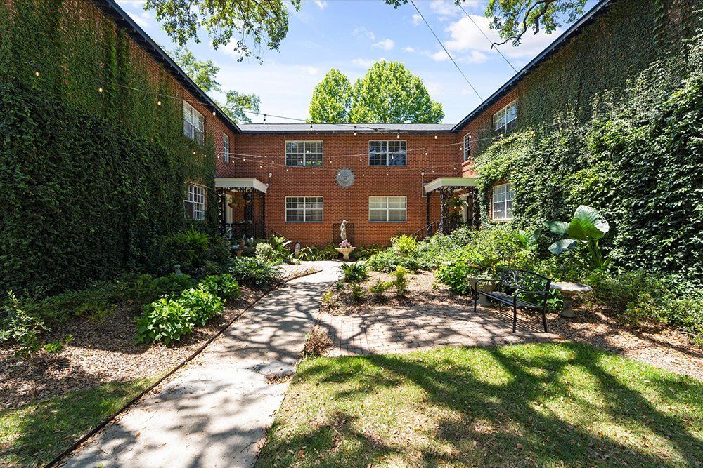 A brick apartment building with a walkway leading to it surrounded by trees and bushes.