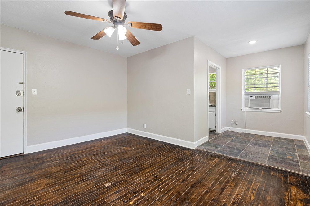 An empty living room with a ceiling fan and a window.