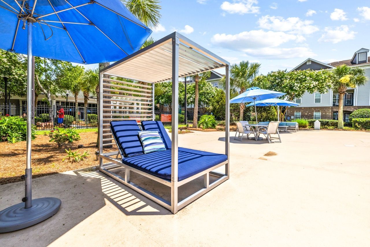 Outdoor community lounge with blue cushioned sunbed under shade and umbrellas.