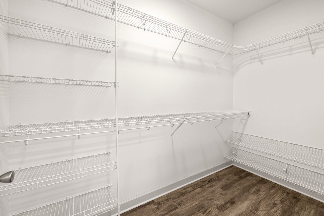 Bright walk-in closet with white wire shelving and dark wood flooring.