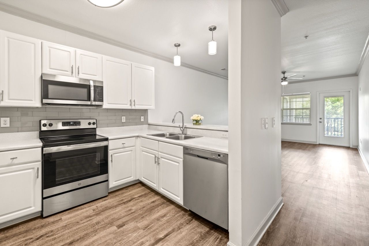 Modern white kitchen with stainless steel appliances, double sink, and light wood flooring.