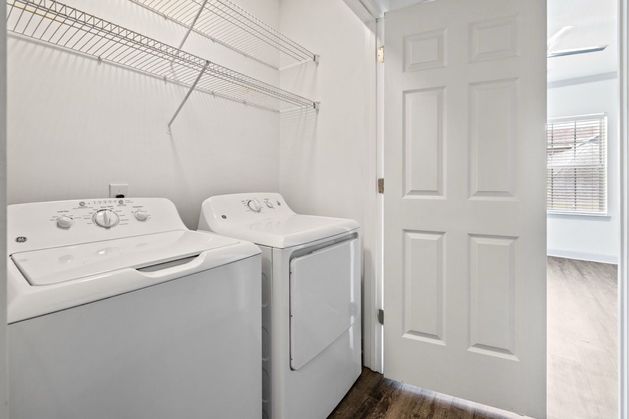White washer and dryer in a laundry closet with wire shelves and an open door.