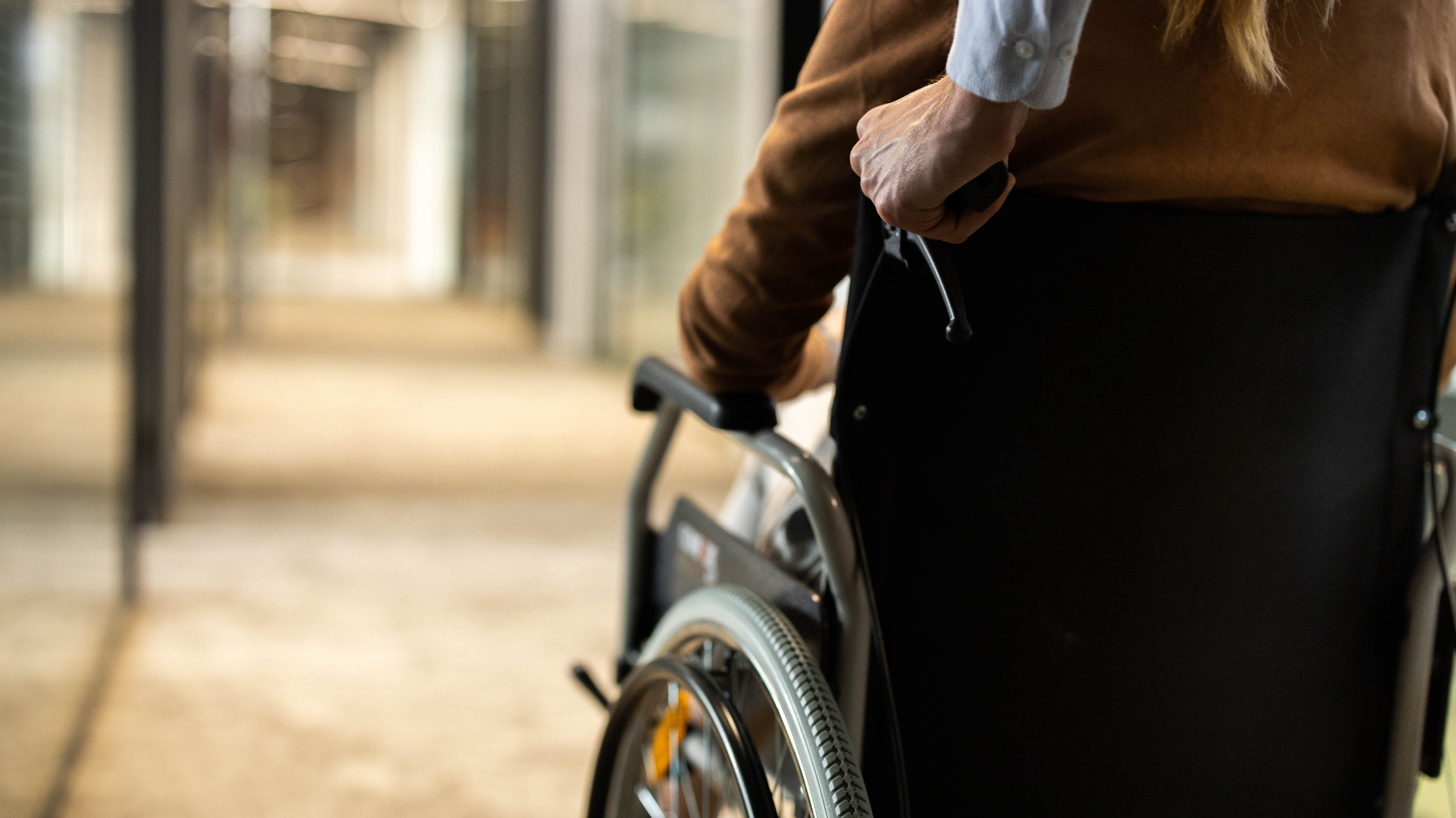 Person in a wheelchair being assisted down a hallway.