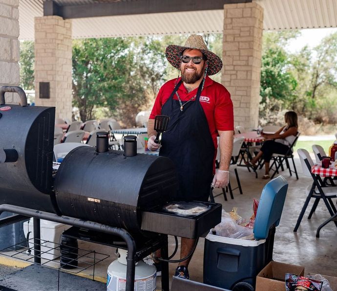 A man wearing a hat and apron is standing in front of a grill.