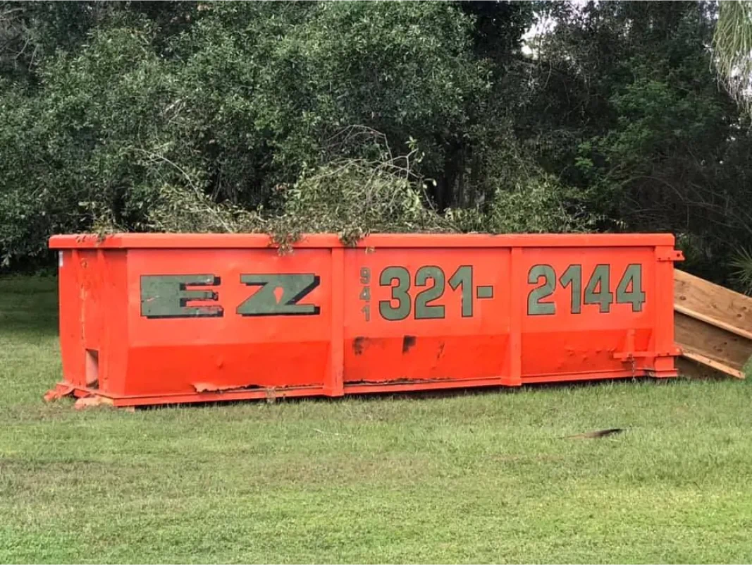 Orange dumpster with EZ logo and 321-2144 phone number on green grass in front of trees.