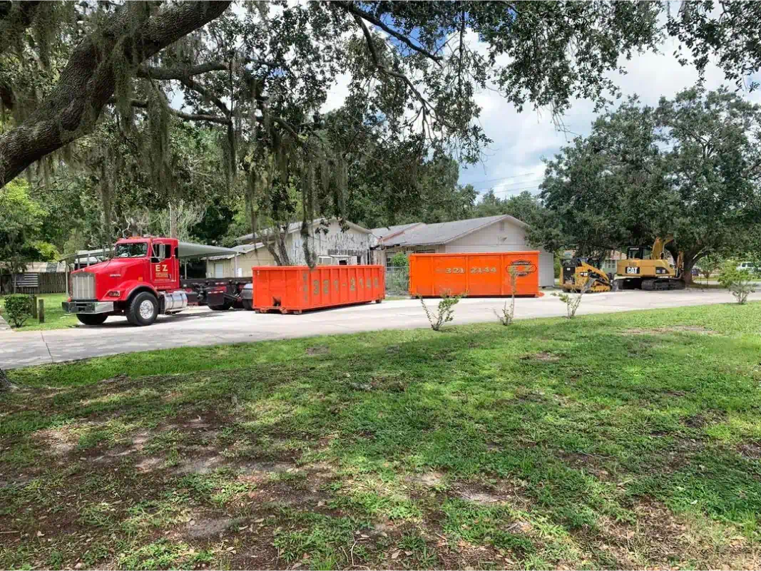 Red truck and orange dumpsters in front of a house, possibly for construction or cleanup.