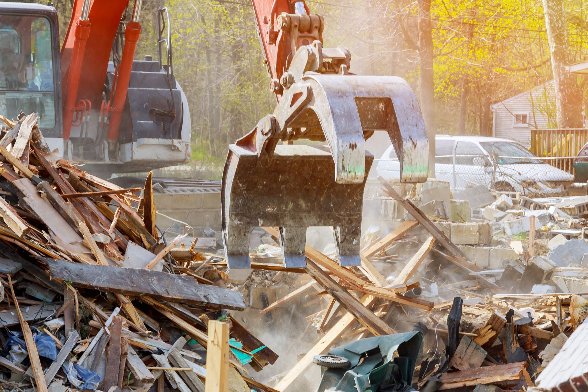 Excavator bucket lifting debris at a demolition site with piles of broken wood and dust
