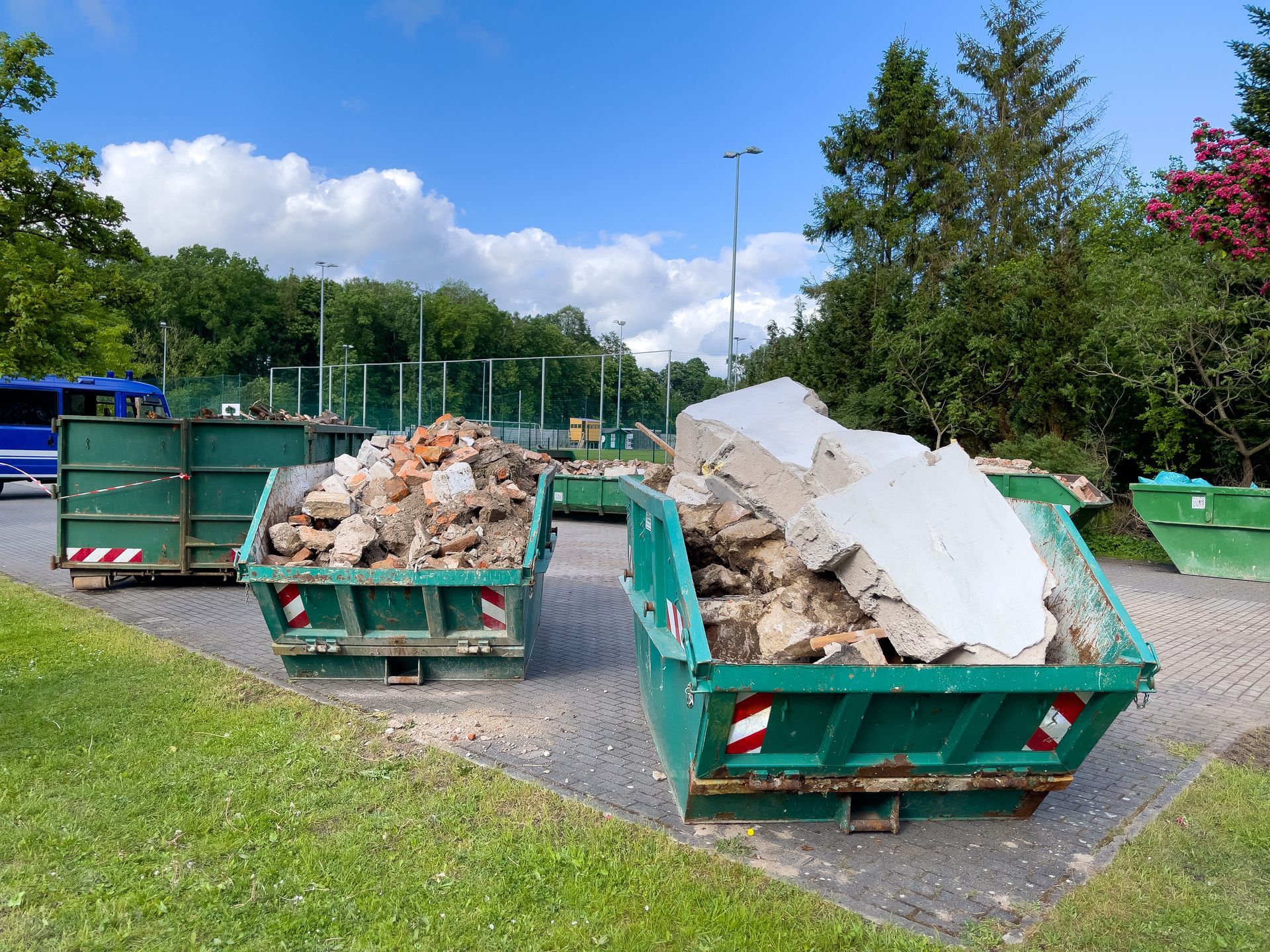 Green dumpsters filled with construction debris in a sunny outdoor lot