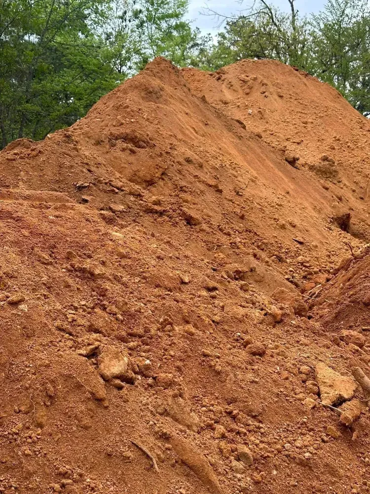 Large reddish-brown dirt pile with green trees in the background