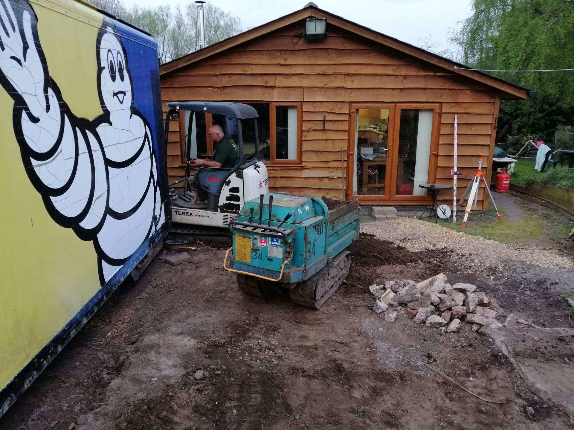 A man is driving a bulldozer in front of a wooden house.