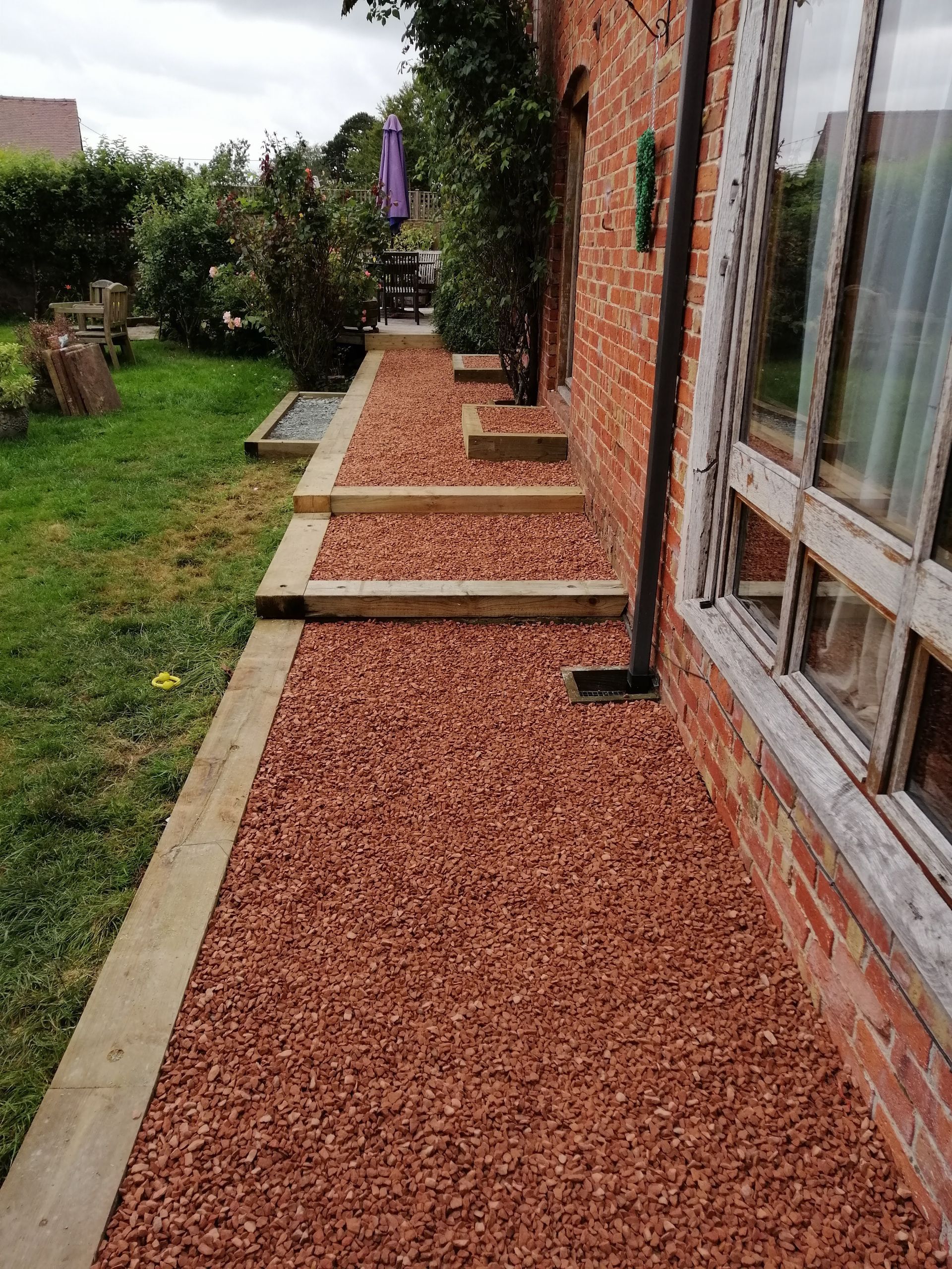 A walkway leading to a brick house with gravel and wooden steps.