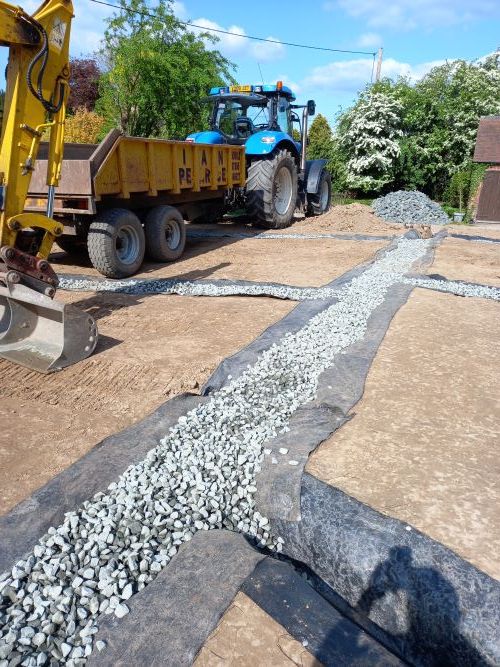 A blue tractor is loading gravel into a yellow dump truck.