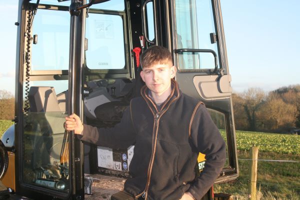 A man in a black jacket is standing in front of a tractor