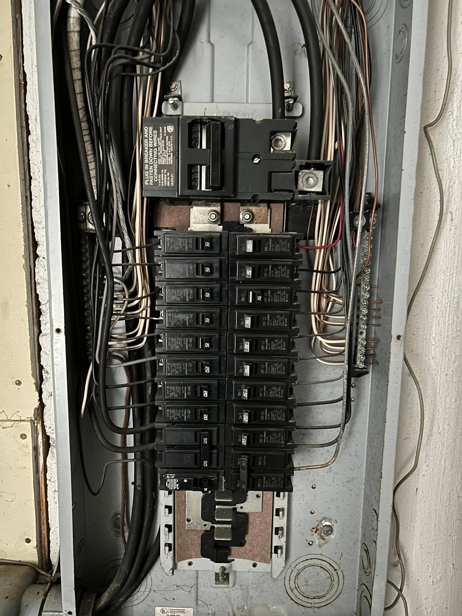 Electrical panel with black circuit breakers and wiring inside a metal box.