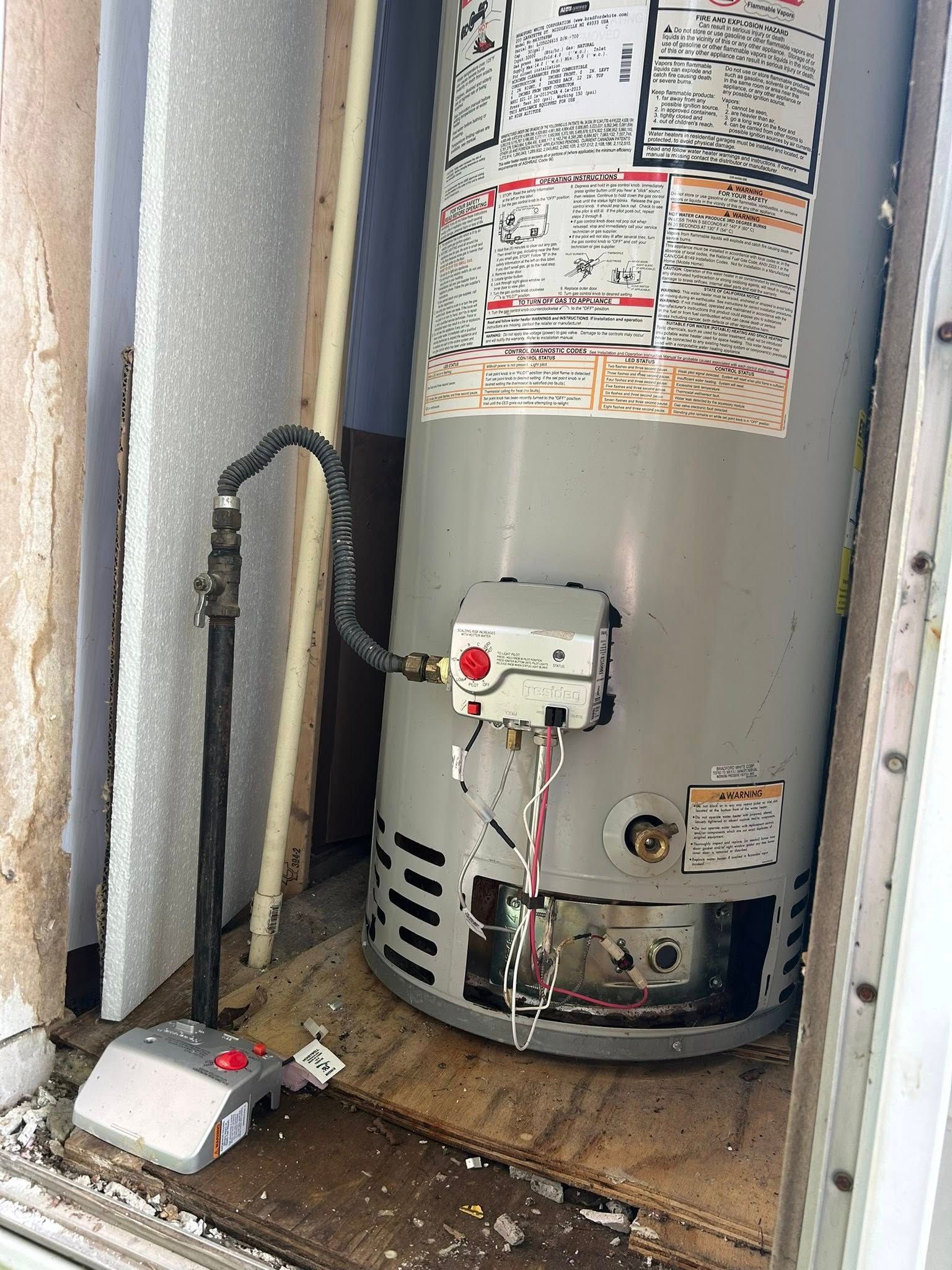 Water heater against a wall with gas line and control panel, in a tight space.