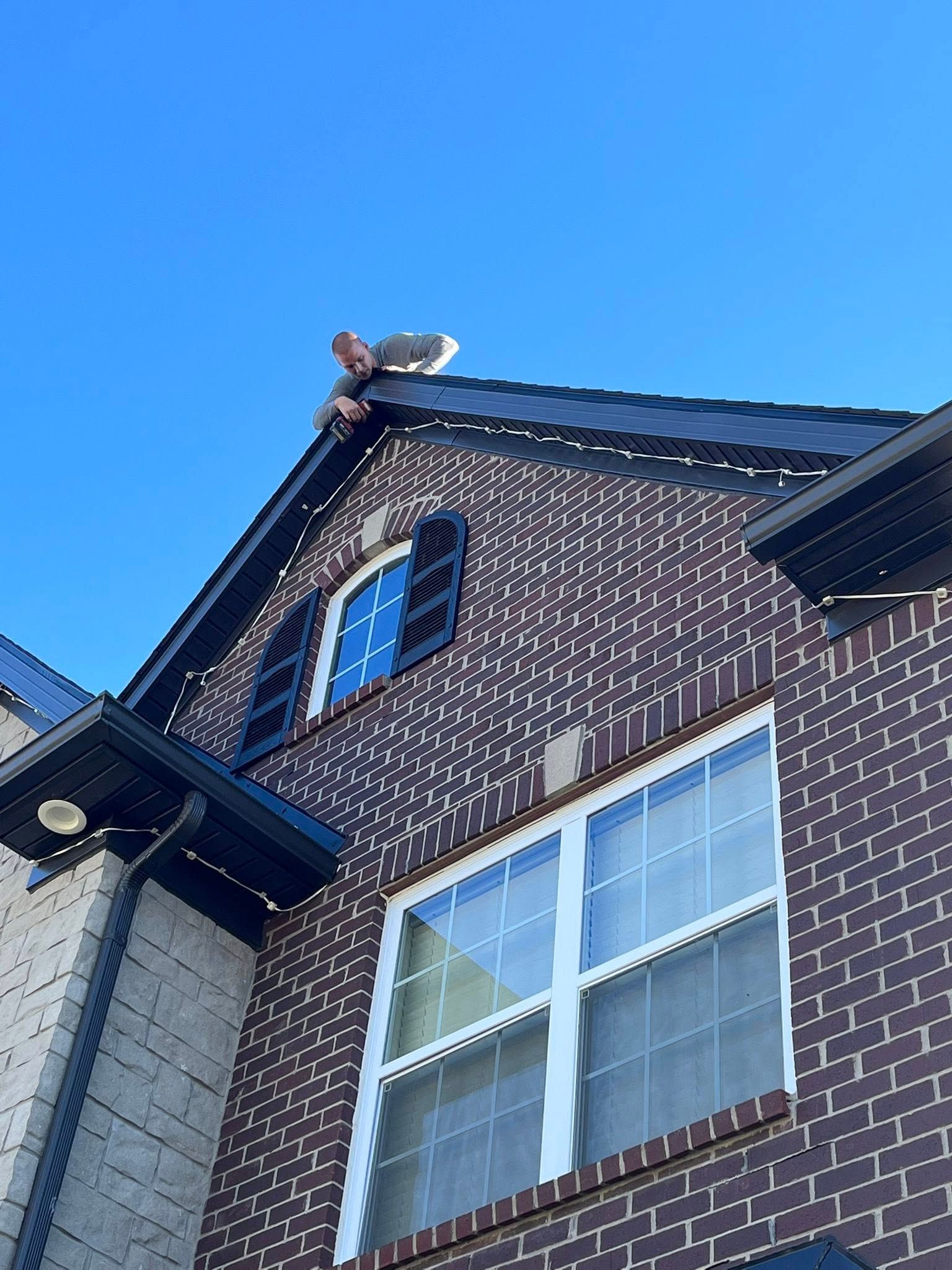 Person on a roof working. Dark brick house, clear blue sky.