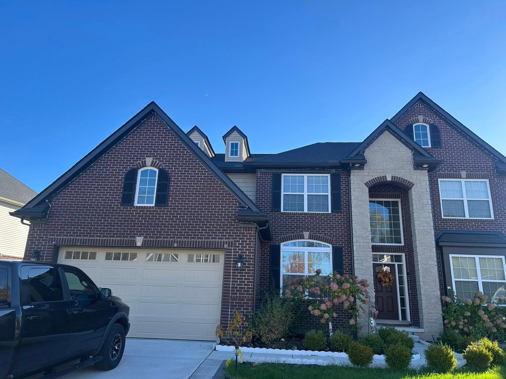 Two-story house with brick and siding, a garage, and a black truck parked in front.