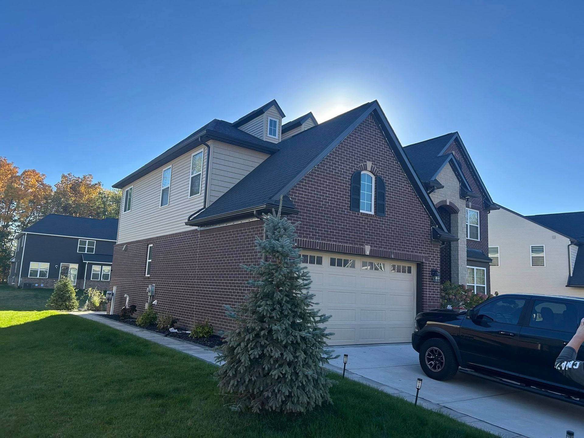 Two-story house with brick and tan siding, a garage, and a black truck on a sunny day.