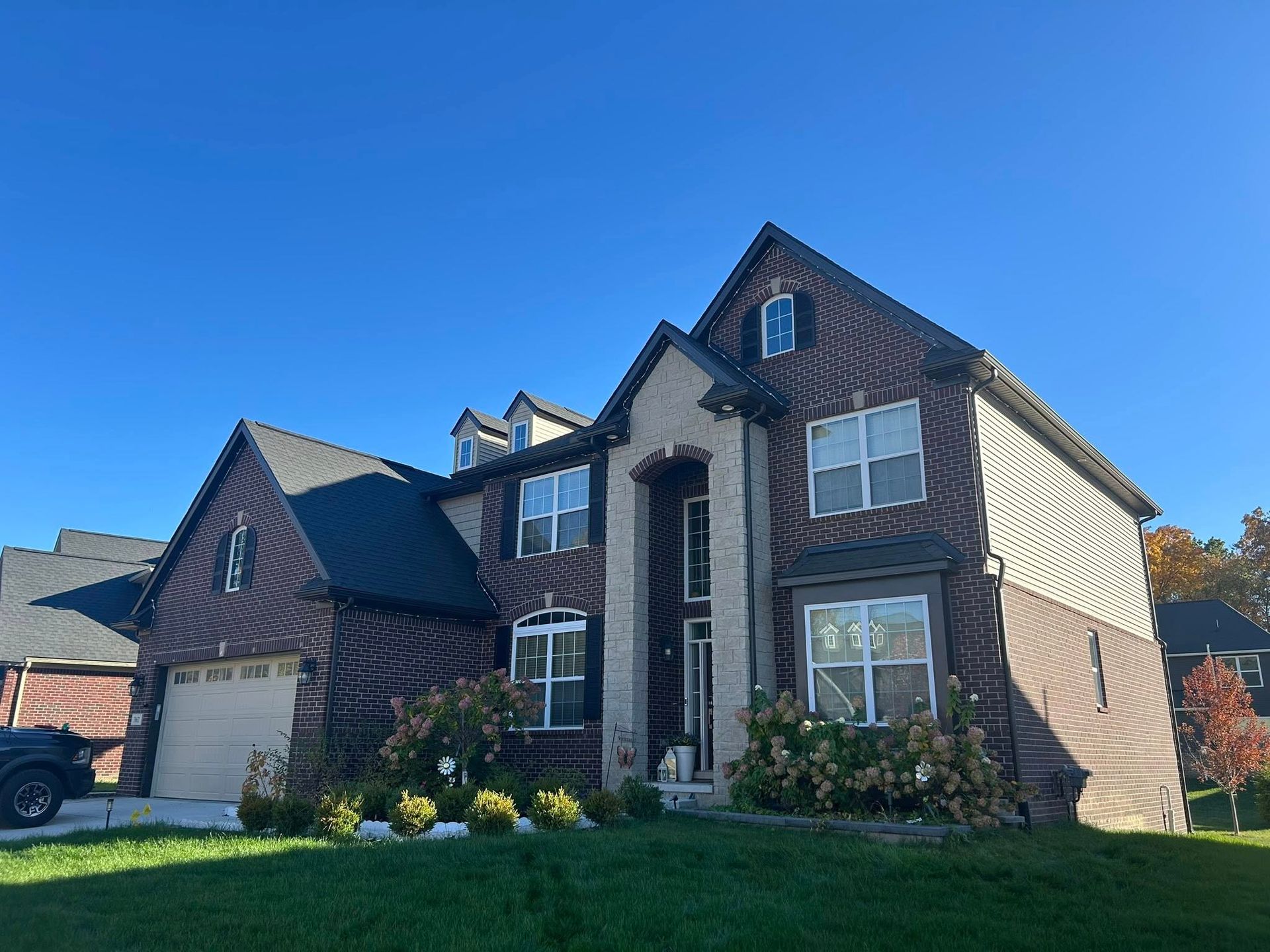 Two-story brick house with brown siding, garage, and green lawn under a blue sky.