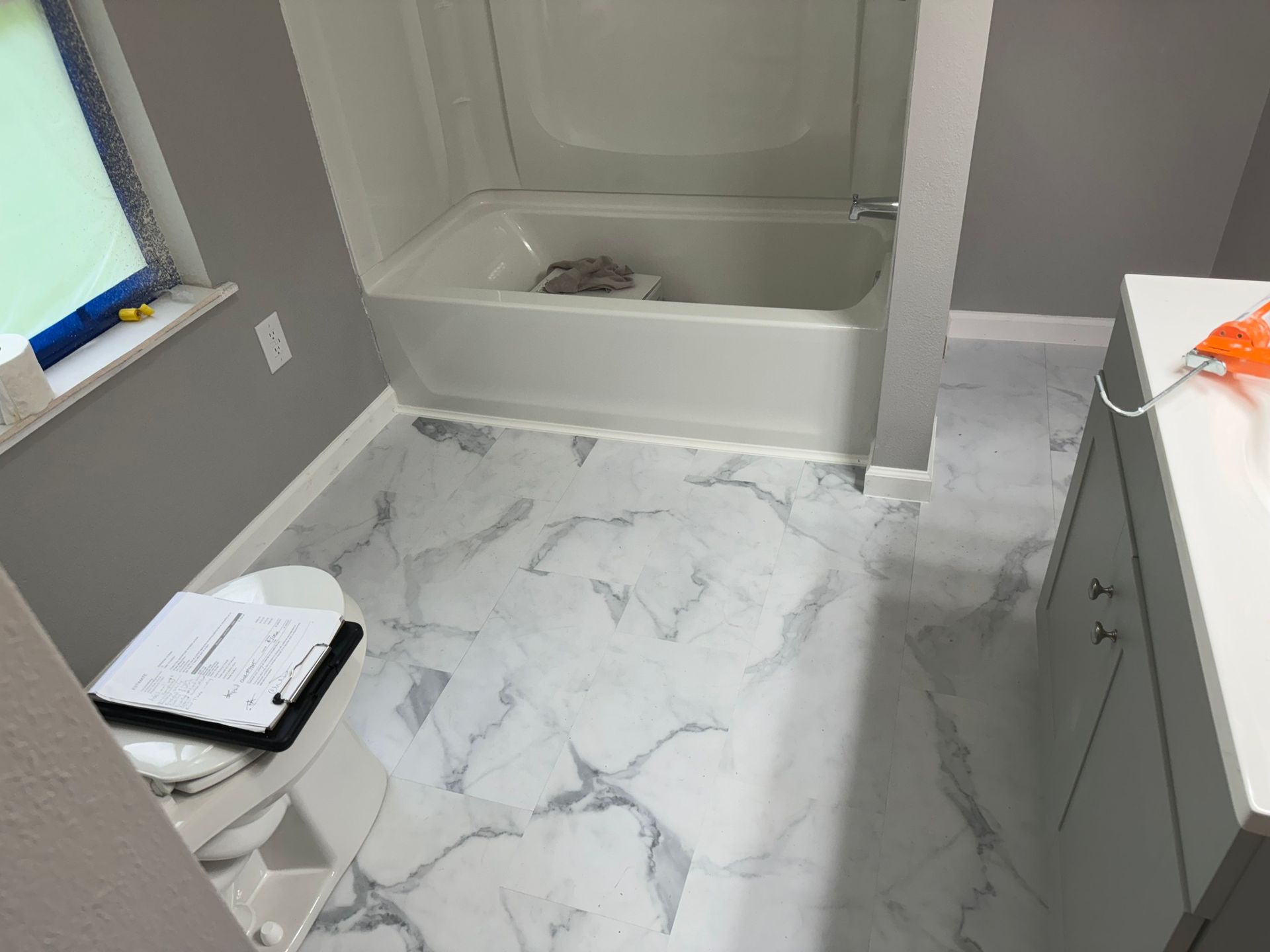 Bathroom with white marble-patterned floor tiles, white bathtub, gray walls, and a white vanity.
