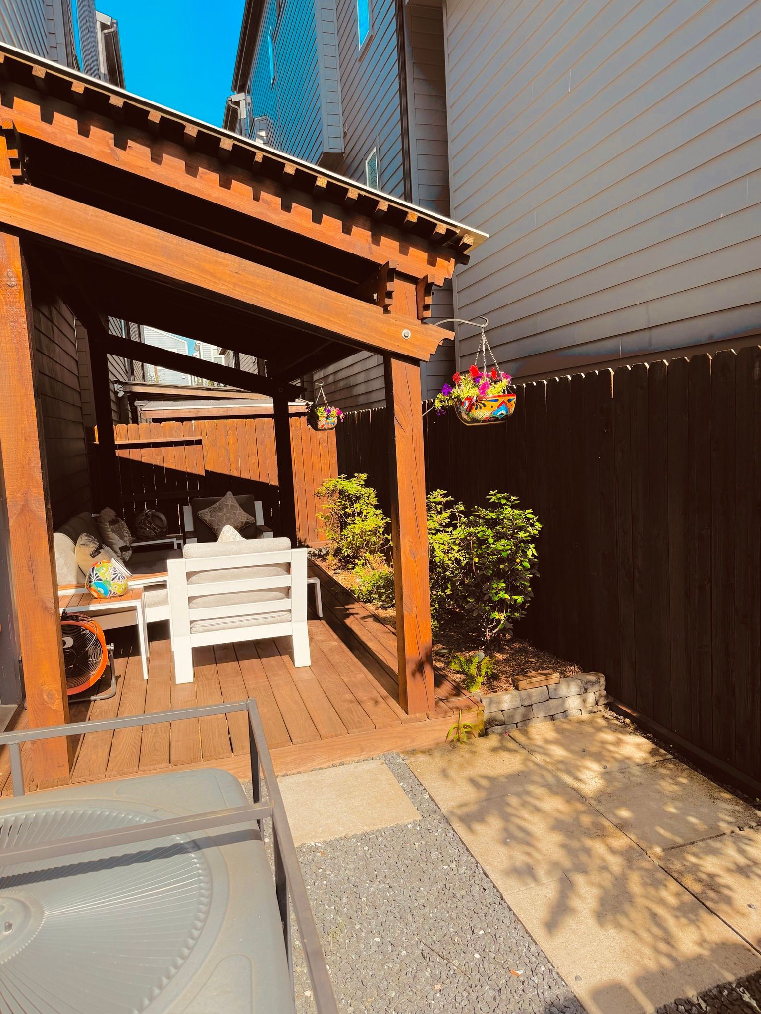 Wooden pergola over a backyard deck with seating, flanked by a wooden fence, and surrounded by foliage.