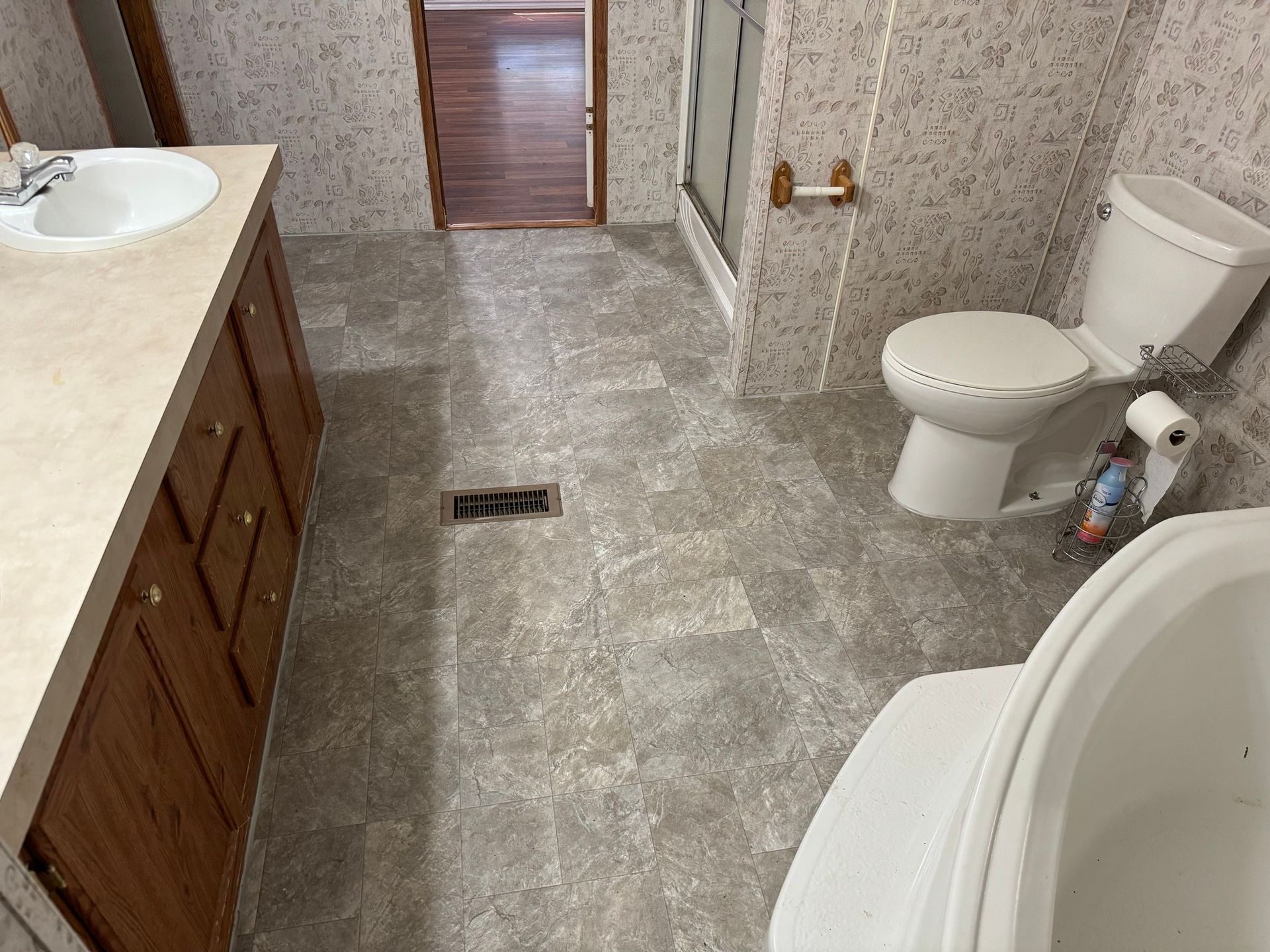 Bathroom with beige countertops, wooden cabinets, gray flooring, and a white toilet and tub.