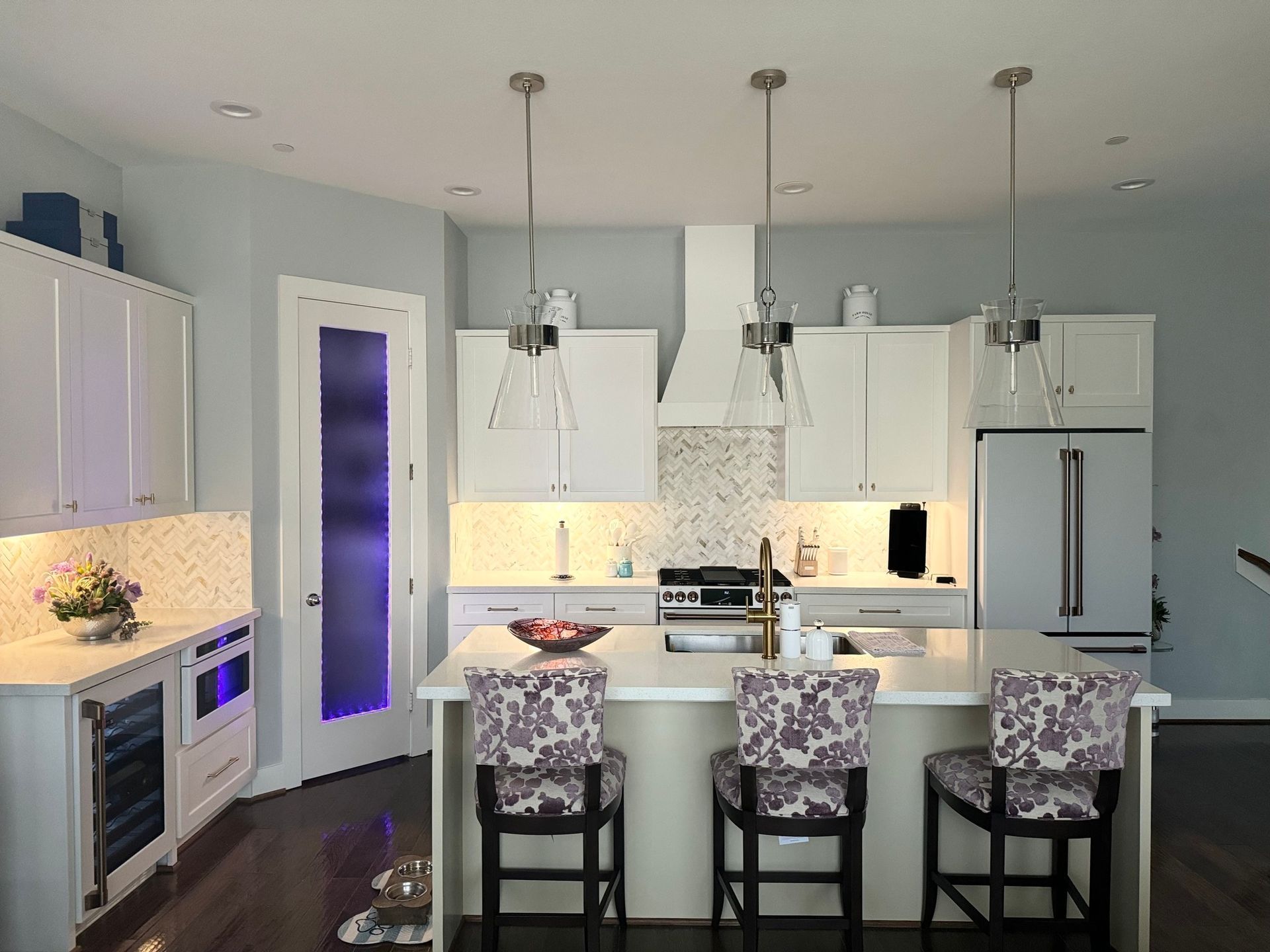 Modern white kitchen with island, pendant lights, and patterned bar stools.