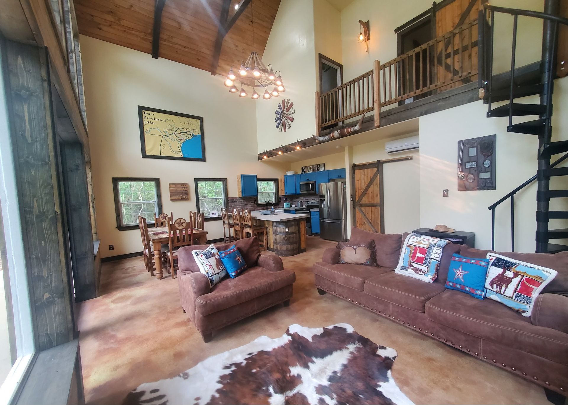 Rustic living room with brown furniture, cowhide rug, spiral staircase, and a loft.