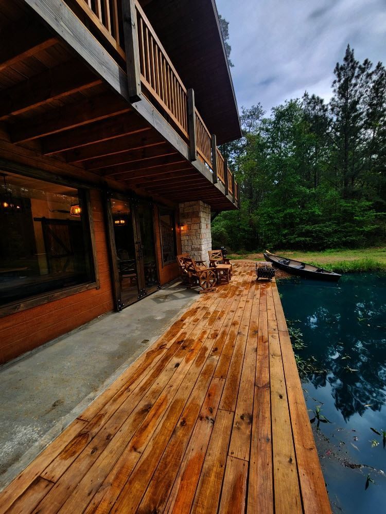 Wooden deck extends to blue pond by rustic two-story cabin with a balcony.