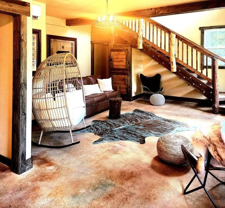 Cozy living room with a wicker chair, brown sofa, wooden staircase, and a cowhide rug.