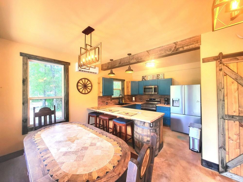 Rustic kitchen and dining room: blue cabinets, wooden accents, barrel island with stools, and a wooden dining table.