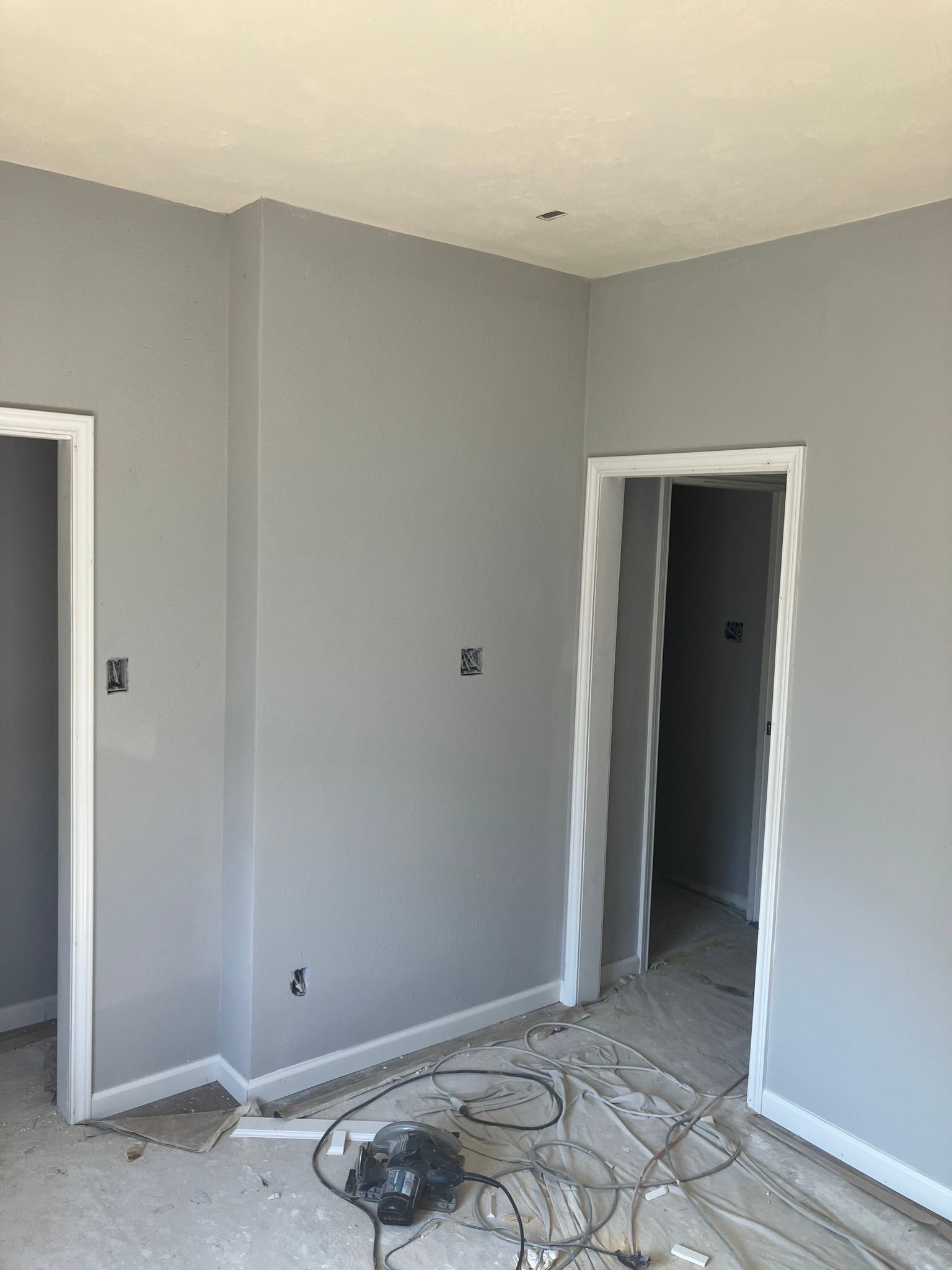 Gray-painted room with white trim around doorways. Electrical wiring and debris on floor.