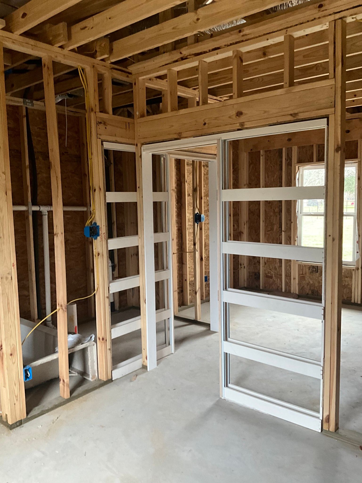 Interior of a building under construction, showing wooden framing and a doorway with white trim.