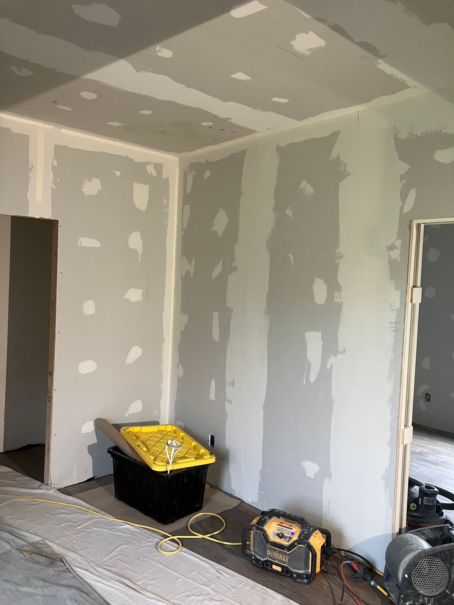 Interior corner of a room with drywall; a yellow tool case and equipment sit on the floor.