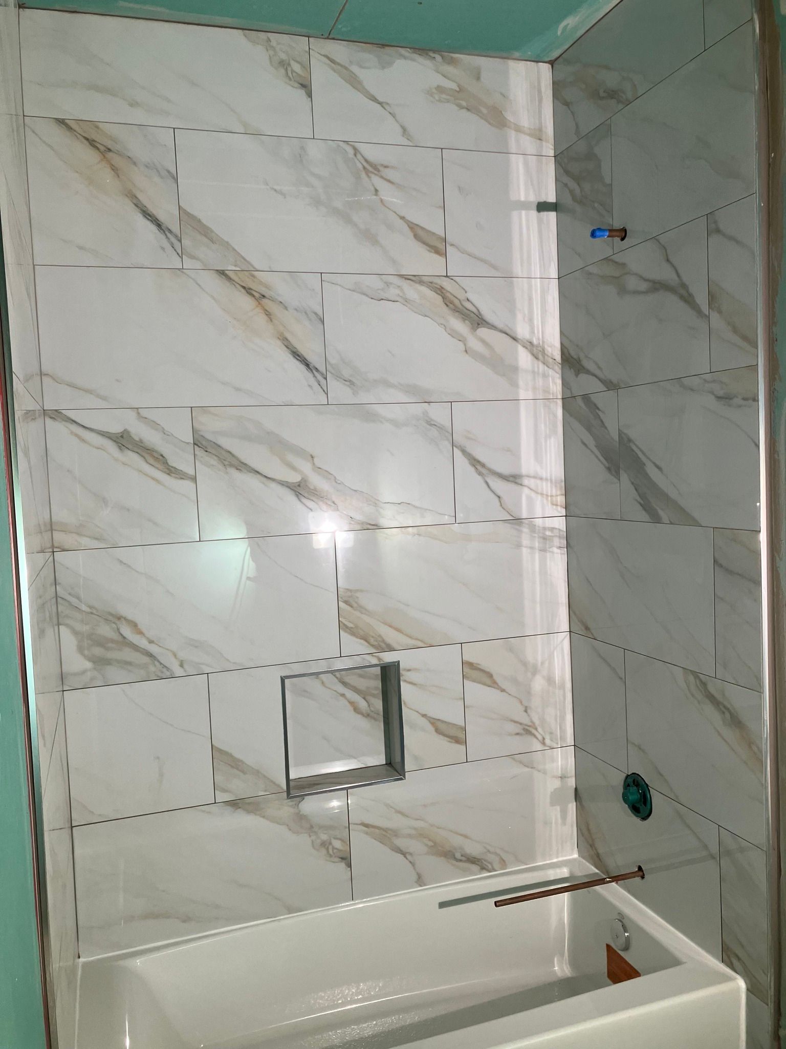 Bathroom with white and gold marble-patterned tiles on the wall above a white bathtub.