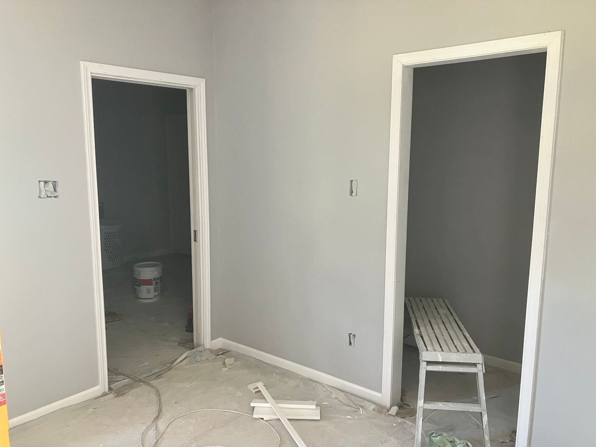 Two doorways in a room with gray walls and white trim. One leads to a closet with a bench.