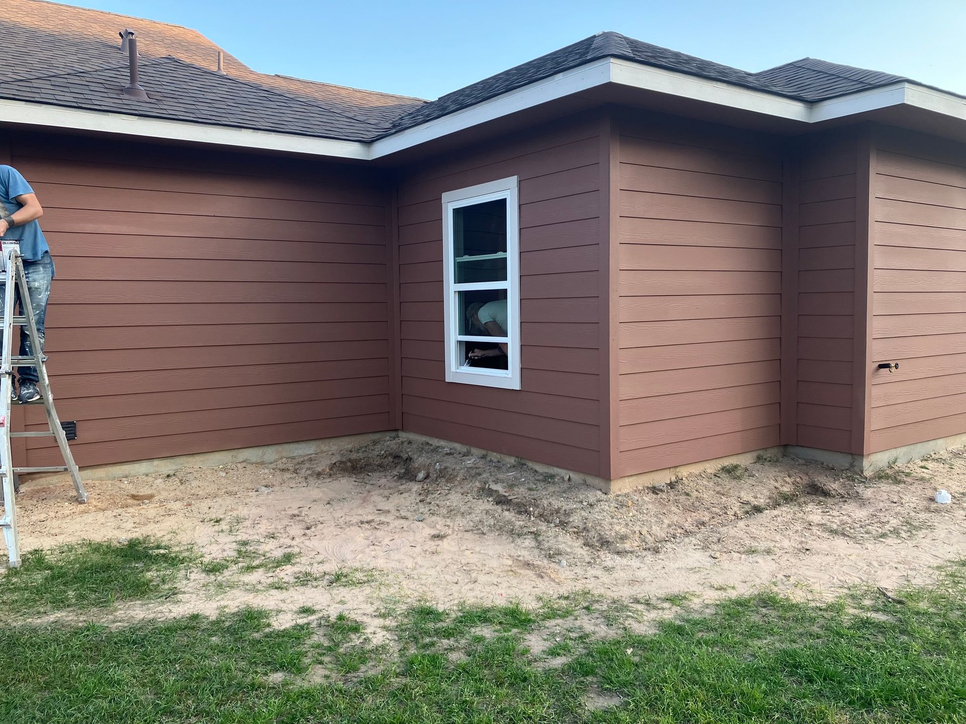 Brown siding installation on a house. A person on a ladder works near a window.