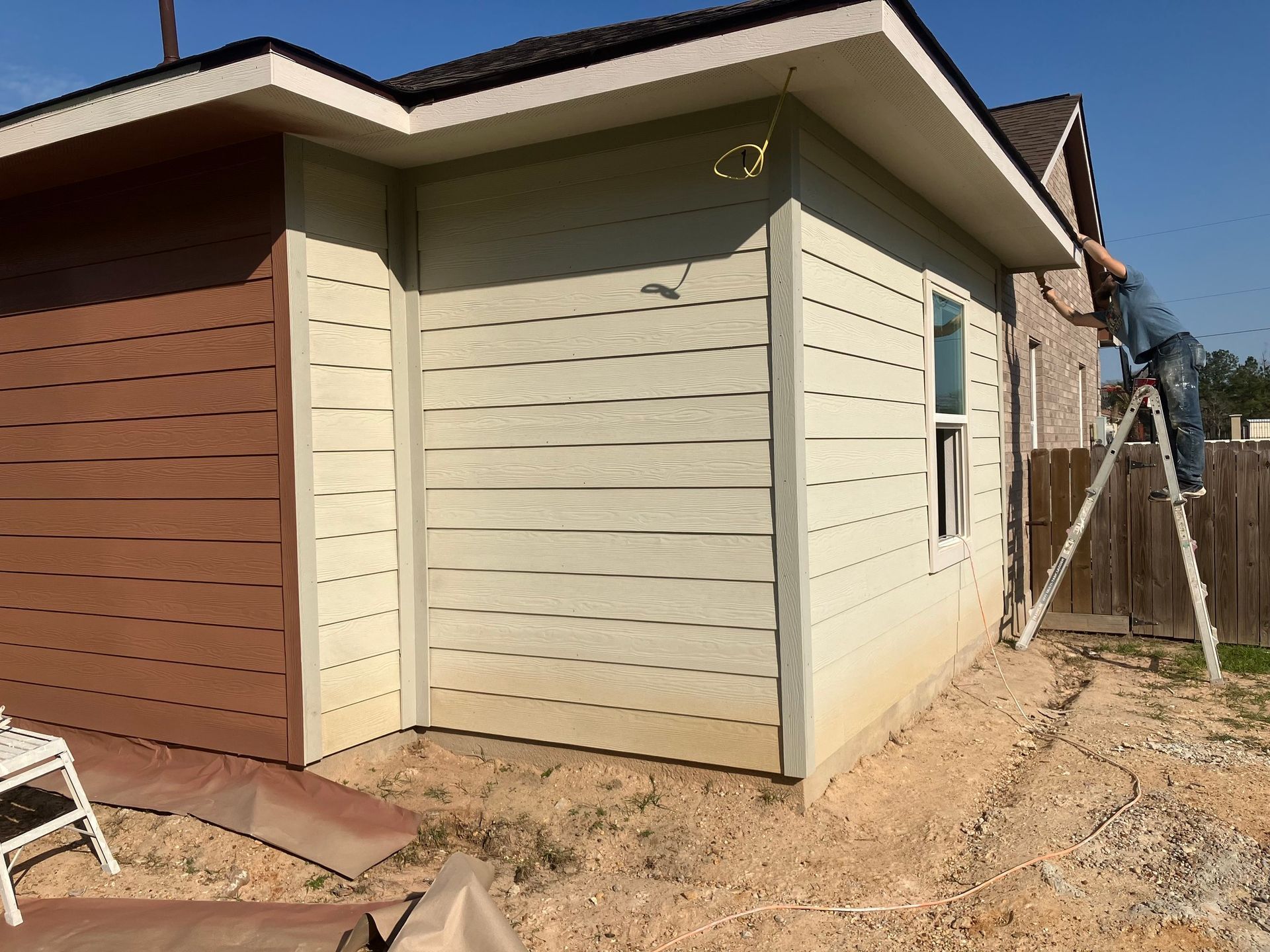 Exterior of a building, siding in two colors, worker on ladder, sunny day.