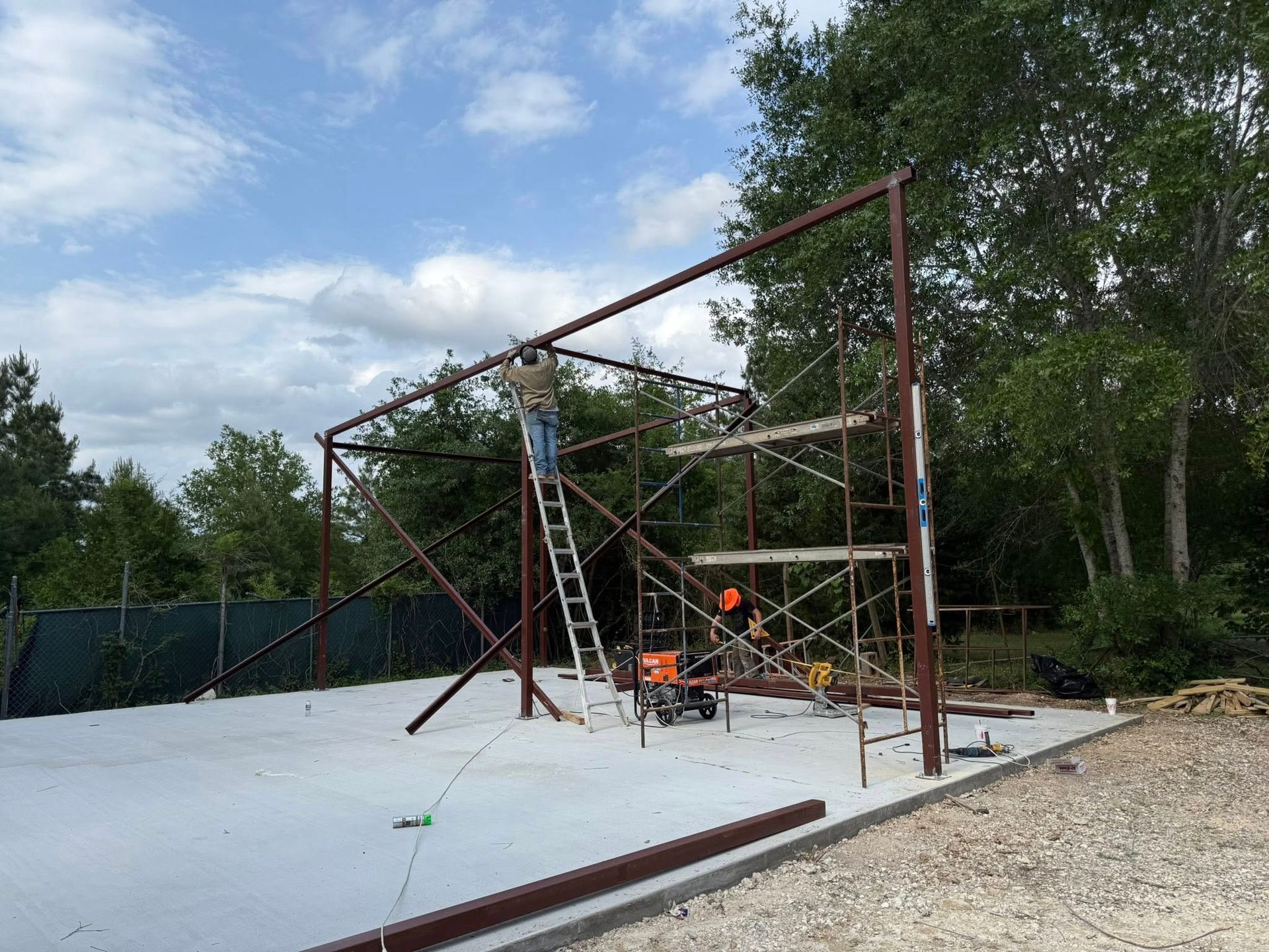 Construction of a metal frame building; workers on ladder and scaffolding, sky above.