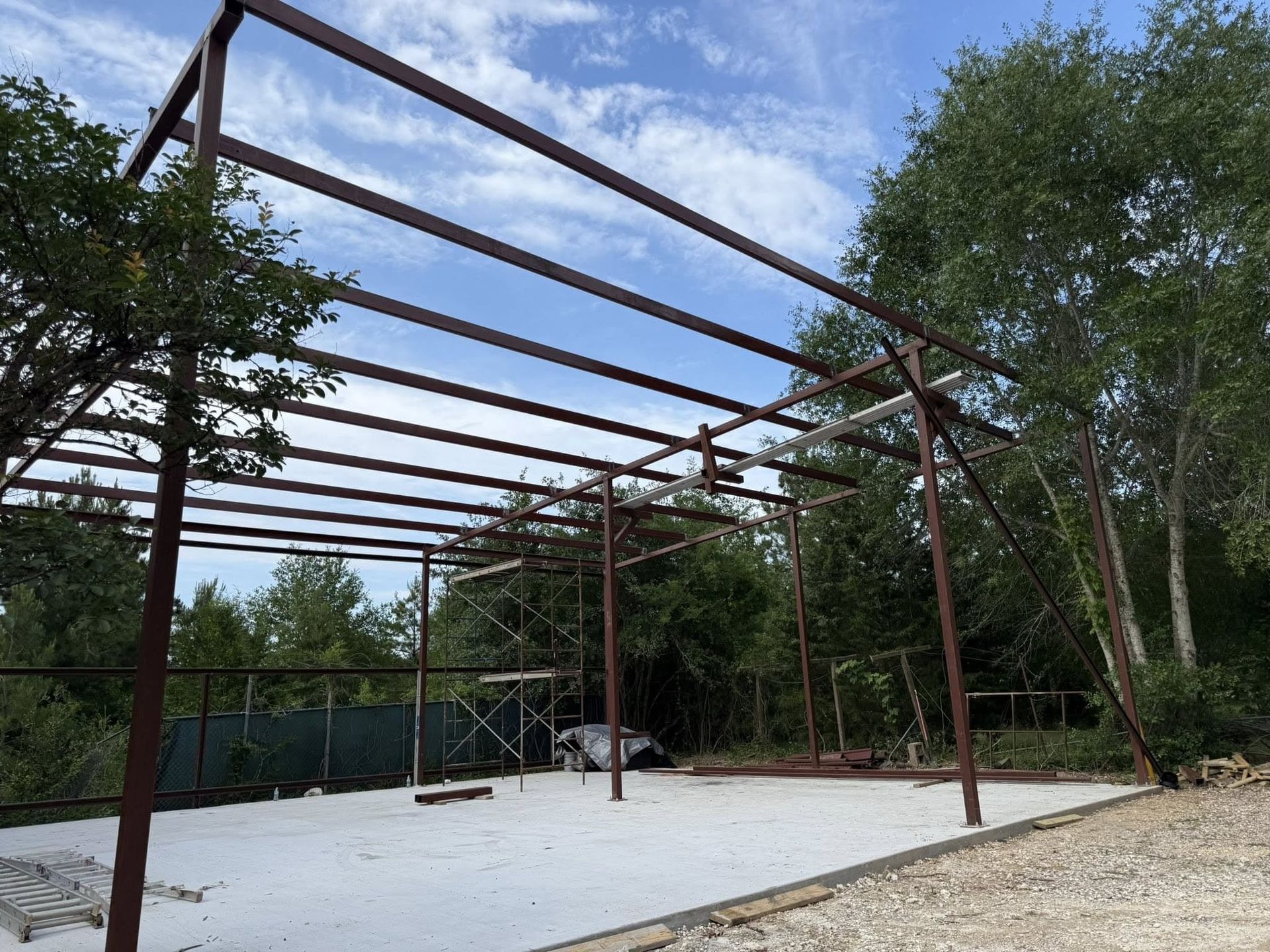 A metal structure is being built in a yard with trees in the background.
