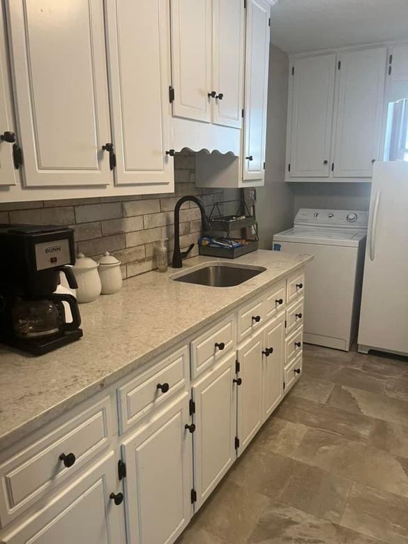 A kitchen with white cabinets , a sink , a washer and dryer , and a refrigerator.