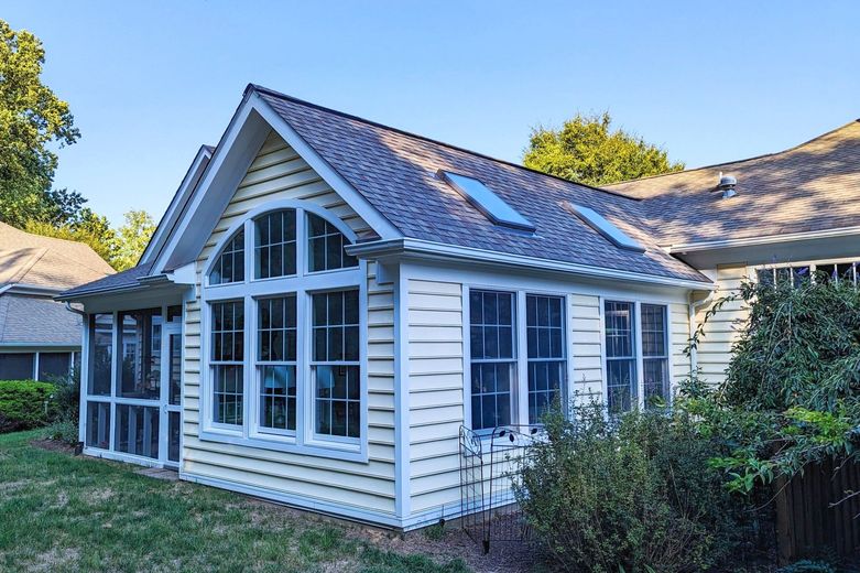 A white house with a screened in porch and a gray roof.