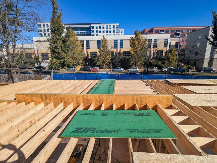 A wooden structure is being built in a city with a building in the background.