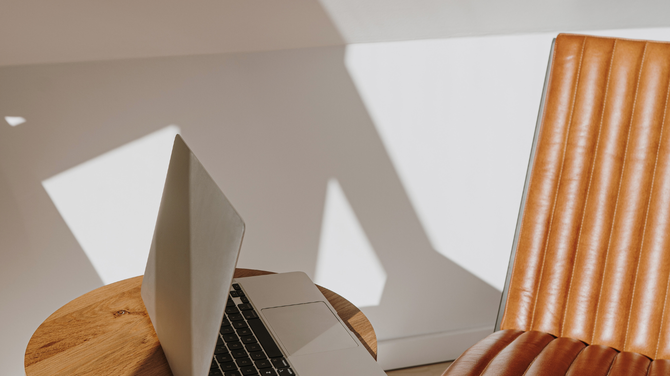 A laptop is sitting on a wooden table next to a chair.